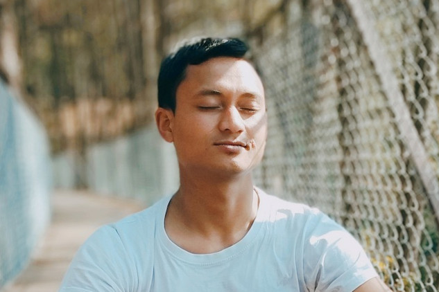 Connecting to Your True Self with the True-Self Breath a man with a peaceful smile sitting in meditation pose outside on a bridge